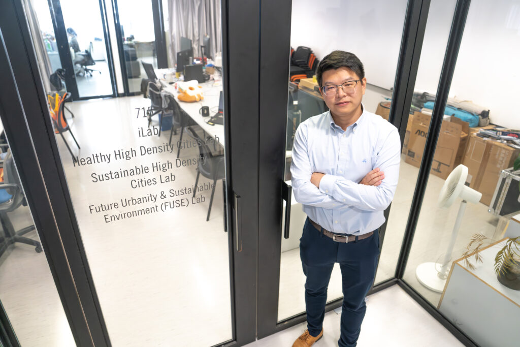 Professor Bin Chen, an expert on satellites, remote sensing, and urban intelligence, poses in front of a sign for his Future Urbanity and Sustainable Environment Lab